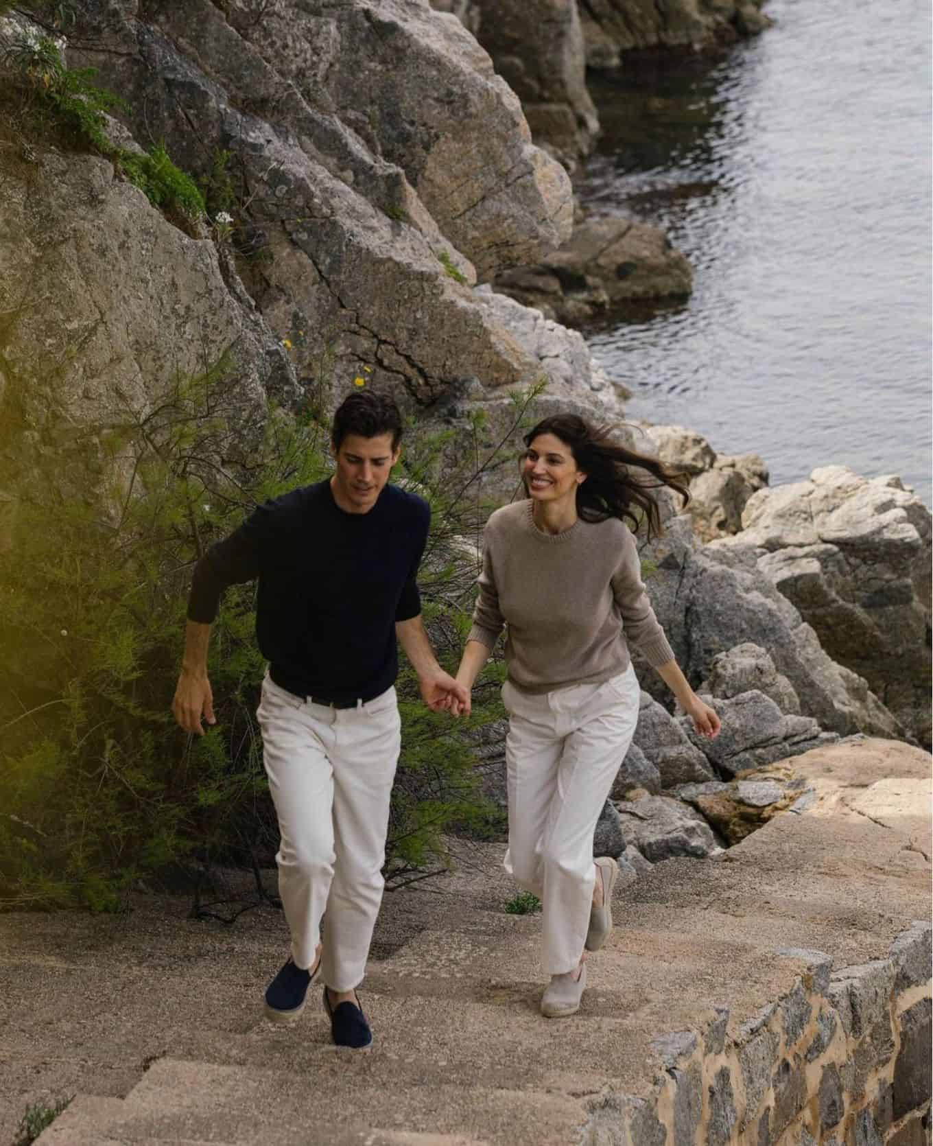Man and woman holding hands running up a path from the ocean