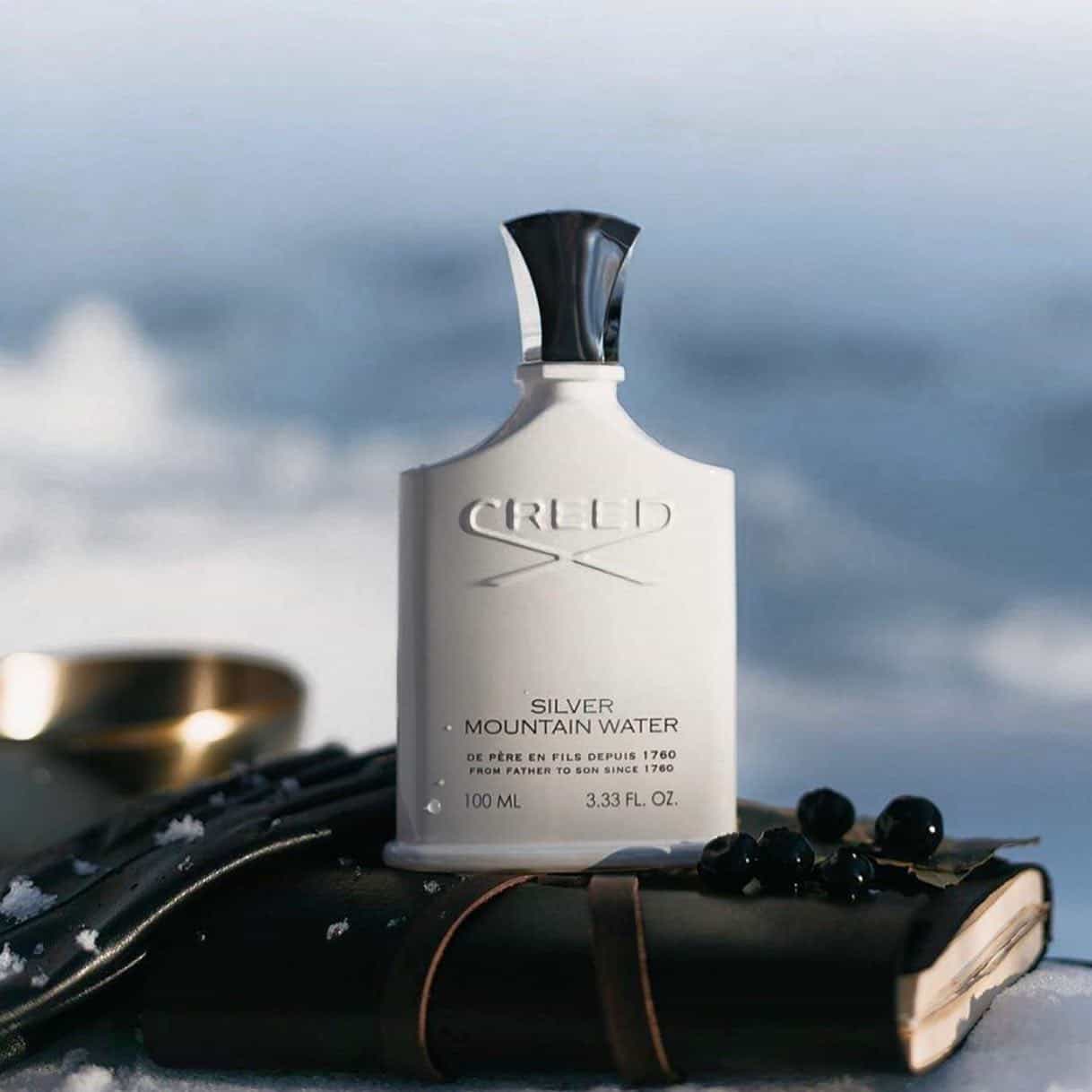 a bottle of creed silver mountain water on top of a leather bound journal