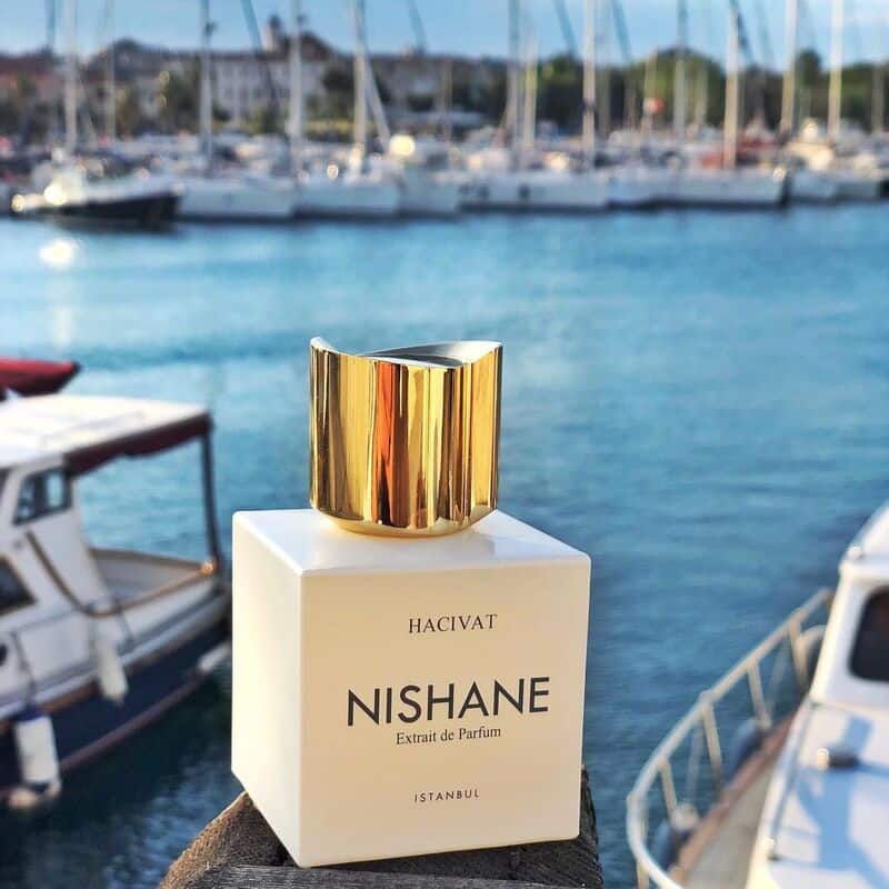 a bottle of Nishane Hacivat perfume at the docks with yachts in the background